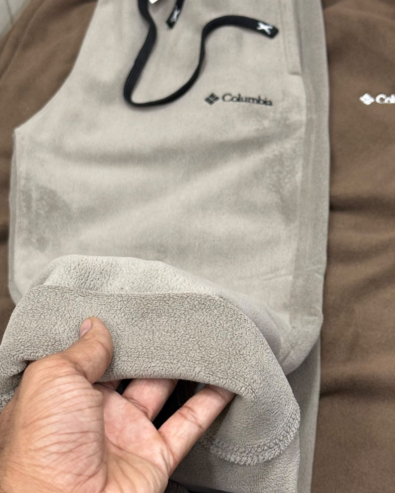Hand turning back the hem of taupe fleece joggers to show the thick brushed fleece inside