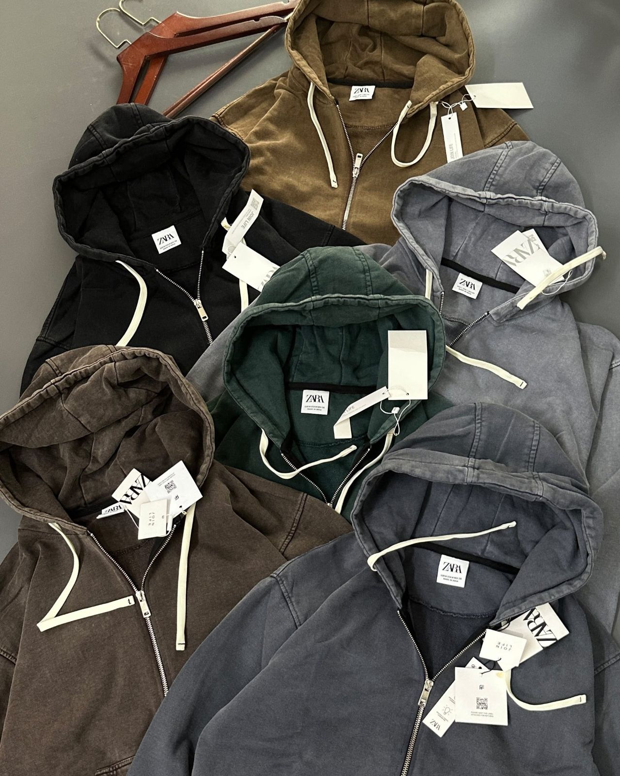 Six washed zip hoodies in olive brown, black, bottle green, slate grey, mocha and charcoal blue laid out together